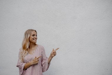 sokakta gri duvara yakın bir şey işaret gülümseyen çekici sarışın kadın