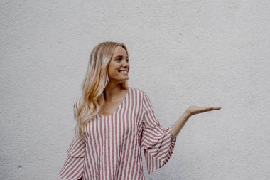 sokakta gri duvara yakın bir şey gösteren gülümseyen çekici sarışın kadın