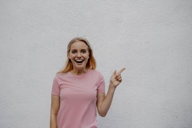 heyecanlı çekici sarışın kadın sokakta gri duvara yakın bir şey işaret