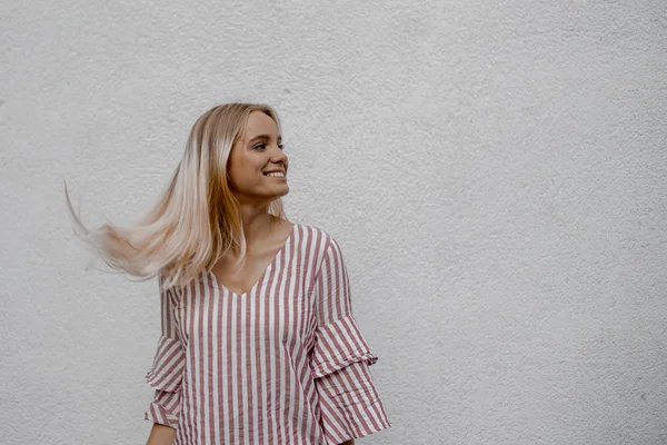 sokakta gri duvarın yakınında uzağa bakan gülümseyen çekici sarışın kadın