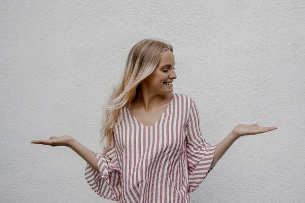 Uśmiechnięta Atrakcyjna Blondynka Pokazując Coś Pobliżu Szarej Ściany Ulicy — Zdjęcie stockowe