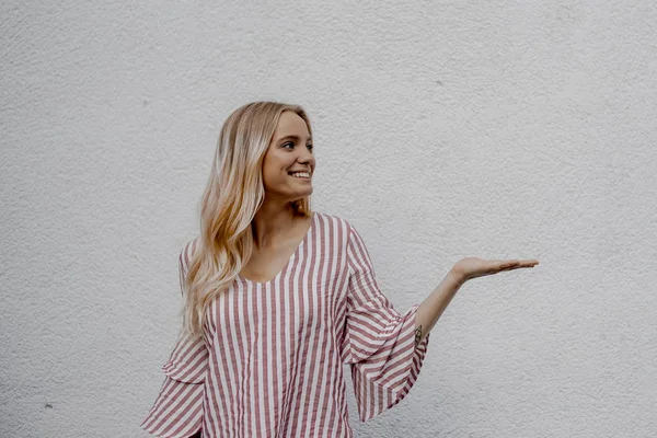 sokakta gri duvara yakın bir şey gösteren gülümseyen çekici sarışın kadın