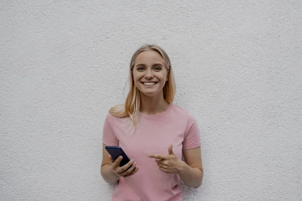 Sorrindo Atraente Mulher Loira Apontando Smartphone Perto Parede Cinza Rua — Fotografia de Stock