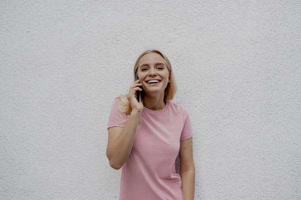 Uśmiechnięta Blondynka Kobieta Mówić Przez Smartphone Pobliżu Szary Ściana Ulicy — Zdjęcie stockowe