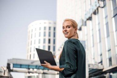 Kız serbest çalışma dizüstü bilgisayarda yazarak ve şehir merkezinde güzel modern kentsel görünümü ile resmi görünümlü. Bilgisayarla seyahat etmek. Online rüya iş, uzaktan çalışma ve serbest kavram