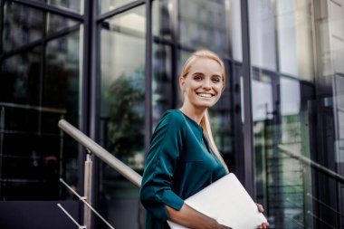 Kendine güvenen ifade güzel genç akıllı sırıtarak profesyonel iş kadını. İş kadını patron, modern ofiste iş toplantısına gidiyor, gri kentsel arka plan.