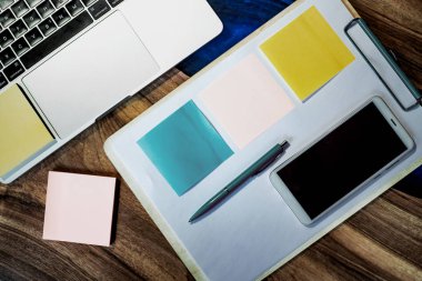 Düz yatıyordu, üst görünüm ofis masa masası. Ahşap masa arka planı üzerinde boş pano, klavye, ofis malzemeleri, kalem, renkli çıkartmalar ve cep telefonu ile çalışma alanı. - Resim