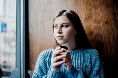 evinin yakınındaki kafede pencere yakınında kahve içen ciddi yüzü olan kadın. Hüzünlü ruh hali, ilham havası. Bazı haberler veya birisi için bekliyorum