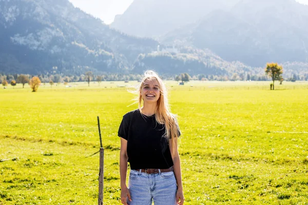 Trekking in the mountains, alpine landscape. Young woman traveler walks on foot green fields at the foot of the high mountains in the countryside. Happy tourist went on tour from the tour operator