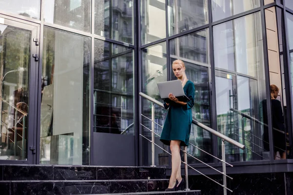 Attractive business woman coming out from modern business center with computer wearing official style after presentation on work meeting, urban space background. Business and finance