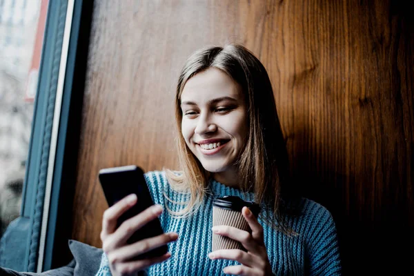 young beautiful woman searching photos on social networks, drinking coffee in local Cafe shop, sitting near window, day off, rest, relax and calm mood