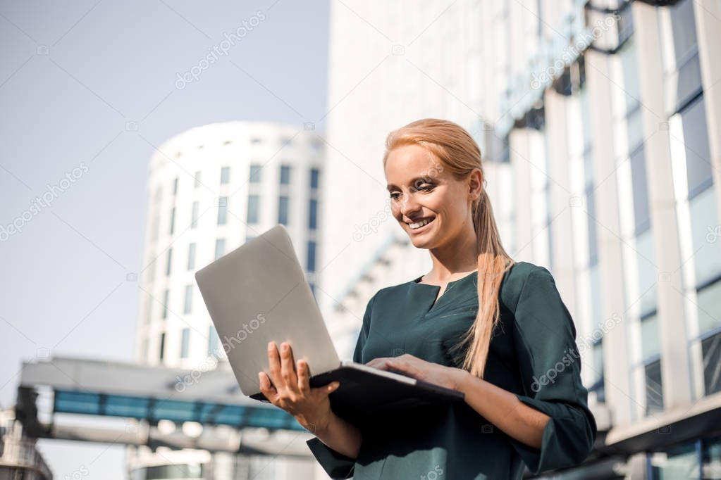 Girl freelancer work typing on laptop and looking official with beautiful modern urban view outdoors at city center. Traveling with a computer. Online dream job, remote work and freelance concept