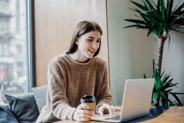 Modern kahve dükkanı sokak şehir kafede oturan modern teknolojileri kullanarak online çalışan güzel kadın blogger, dizüstü bilgisayar ve kahve fincan ı savuruyor. Bloglama, serbest çalışan, uzaktan çalışma