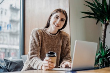 Modern kahve dükkanı sokak şehir kafede oturan modern teknolojileri kullanarak online çalışan güzel kadın blogger, dizüstü bilgisayar ve kahve fincan ı savuruyor. Bloglama, serbest çalışan, uzaktan çalışma