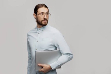 Genç gülümseyen iş adamı ayakta ve dizüstü bilgisayar kullanarak gri arka plan üzerinde izole. İyi ve mutlu görünüyor. Programlama projeleri için çok yeni fikirlerolması