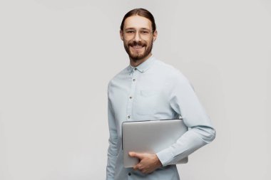 Genç gülümseyen iş adamı ayakta ve dizüstü bilgisayar kullanarak gri arka plan üzerinde izole. İyi ve mutlu görünüyor. Programlama projeleri için çok yeni fikirlerolması 