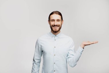 İşte burada! Logonuz için boş kopyalama alanı. Gri duvar arka plan üzerinde izole ayakta mutlu genç adam fotoğrafı. Copyspace'i gösteren kameraya bakın. İnsanlar duygu kavramı 