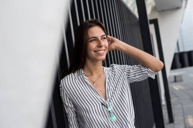 Gülümseyen neşeli uzun saçlı kız tam bir göğüs nefes ve özgürlük sahiptir, kentsel duvar yanında duruyor. Beyaz bluz la sevimli genç kadının portresi dışarıda eğleniyor