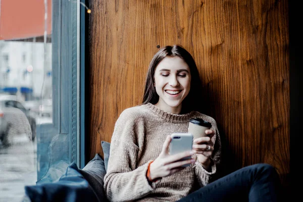 beautiful woman searching photos on social networks, drinking coffee in local Cafe shop, sitting near window, day off, rest, relax and calm mood