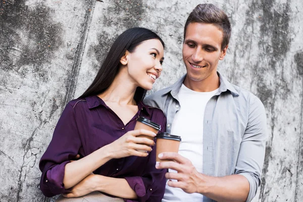 Hurry for meeting. Two young business people walking outside on the city street drinking hot coffee talking smiling joyful close-up. Romantice relationship, love affair at work