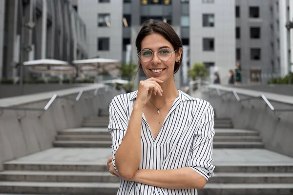 Happy woman manager thinking about something good while standing outdoor modern office business center, young smart female secretary smiling for someone, confident successful woman