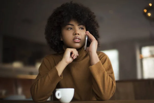 An important phone conversation, a young beautiful African American woman has a call for work from her boss, she is focused and serious. She has a lunch break, she sits in a coffee shop with a coffee