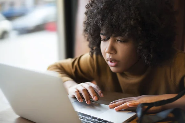 A young worker, an intern, an african-american woman, works for a laptop, searches for information through the use of Internet resources, social networking. Work at the computer in the office