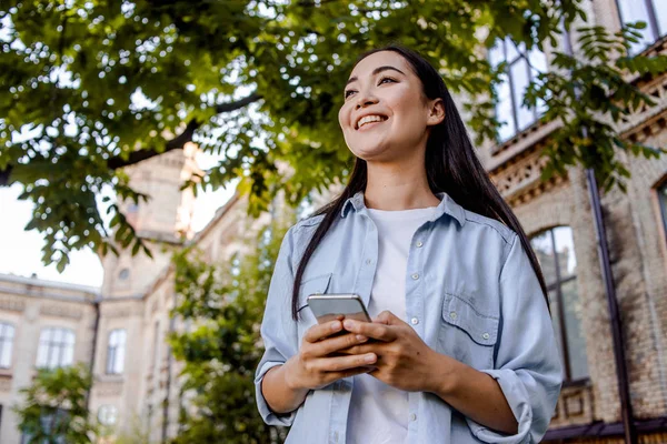 亚洲妇女步行户外与手机 在智能手机上听音乐和观看视频 白色耳机 生活方式概念 使用现代在线互联网技术的学生 — 图库照片