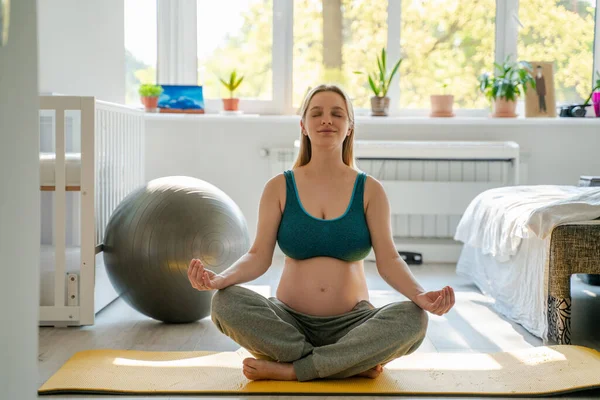 A pregnant woman at home in the morning does exercise exercises from yoga for concentration and relaxation, prepares for motherhood and the birth of a child, preparation for childbirth