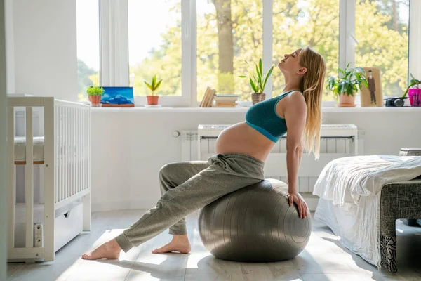 妊娠9ヶ月目に丸い腹を持つ運動妊娠中のスリムな女性は 自宅でスポーツに従事しています 体操や灰色のボールにストレッチ — ストック写真