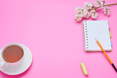 genç bir çocuğun masanın üst görünümü, kalem defter çiçek kompozisyon pembe arka plan üzerinde içecek bir bardak