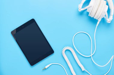 mavi arka plan üzerinde gadget'lar üzerine üst görünüm, beyaz kulaklık ve tablet kompozisyonu