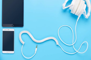 mavi arka plan, beyaz kulaklık, tablet ve telefon kompozisyonu üzerinde gadget'lar üzerine üst görünüm