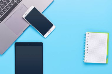 mavi arka plan üzerinde gadget'lar üzerine üst görünüm, bir dizüstü bilgisayar kompozisyonu, beyaz kulaklıklar, telefon, bir içki ve araba anahtarları ile cam