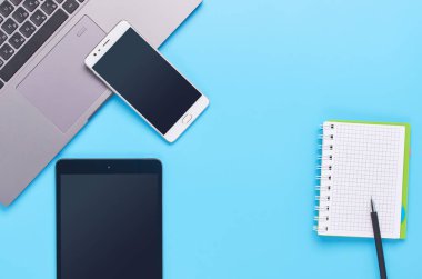 mavi arka plan üzerinde gadget'lar üzerine üst görünüm, bir dizüstü bilgisayar kompozisyonu, beyaz kulaklıklar, telefon, bir içki ve araba anahtarları ile cam