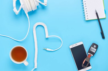 mavi arka plan üzerinde gadget'lar üzerine üst görünüm, beyaz kulaklık kompozisyonu, telefon, tablet, bir içki ve araba anahtarları ile cam