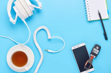 mavi arka plan üzerinde gadget'lar üzerine üst görünüm, beyaz kulaklık kompozisyonu, telefon, tablet, bir içki ve araba anahtarları ile cam