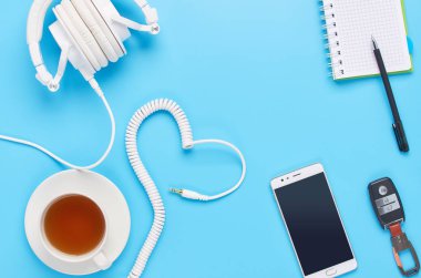 mavi arka plan üzerinde gadget'lar üzerine üst görünüm, beyaz kulaklık kompozisyonu, telefon, tablet, bir içki ve araba anahtarları ile cam