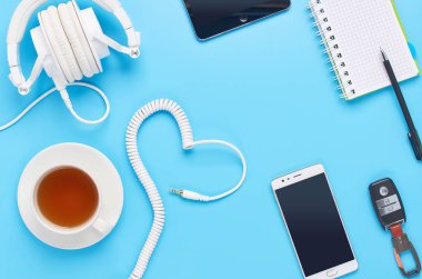 mavi arka plan üzerinde gadget'lar üzerine üst görünüm, beyaz kulaklık kompozisyonu, telefon, tablet, bir içki ve araba anahtarları ile cam