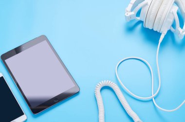 mavi arka plan, beyaz kulaklık, tablet ve telefon kompozisyonu üzerinde gadget'lar üzerine üst görünüm