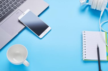 mavi arka plan üzerinde gadget'lar üzerine üst görünüm, bir dizüstü bilgisayar kompozisyonu, beyaz kulaklıklar, telefon, bir içki ve araba anahtarları ile cam
