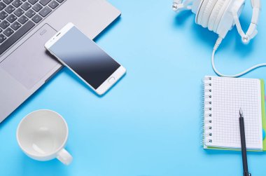mavi arka plan üzerinde gadget'lar üzerine üst görünüm, bir dizüstü bilgisayar kompozisyonu, beyaz kulaklıklar, telefon, bir içki ve araba anahtarları ile cam