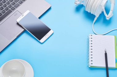 mavi arka plan üzerinde gadget'lar üzerine üst görünüm, bir dizüstü bilgisayar kompozisyonu, beyaz kulaklıklar, telefon, bir içki ve araba anahtarları ile cam