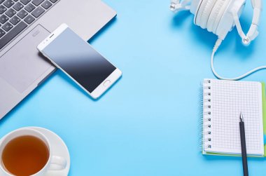 mavi arka plan üzerinde gadget'lar üzerine üst görünüm, bir dizüstü bilgisayar kompozisyonu, beyaz kulaklıklar, telefon, bir içki ve araba anahtarları ile cam