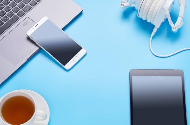 mavi arka plan üzerinde gadget'lar üzerine üst görünüm, bir dizüstü bilgisayar kompozisyonu, beyaz kulaklıklar, telefon, bir içki ve araba anahtarları ile cam