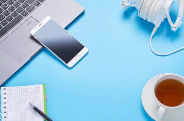 mavi arka plan üzerinde gadget'lar üzerine üst görünüm, bir dizüstü bilgisayar kompozisyonu, beyaz kulaklıklar, telefon, bir içki ve araba anahtarları ile cam