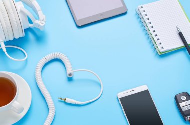 mavi arka plan üzerinde gadget'lar üzerine üst görünüm, beyaz kulaklık kompozisyonu, telefon, tablet, bir içki ve araba anahtarları ile cam