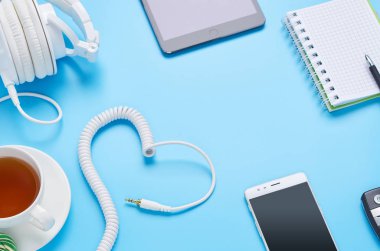 mavi arka plan üzerinde gadget'lar üzerine üst görünüm, beyaz kulaklık kompozisyonu, telefon, tablet, bir içki ve araba anahtarları ile cam
