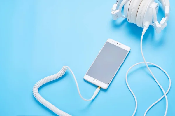 Vista superior sobre gadgets sobre fondo azul, composición de auriculares blancos y teléfono — Foto de Stock
