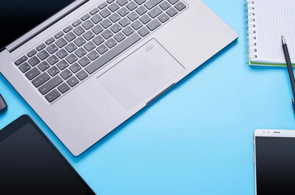 Vista superior sobre gadgets sobre fondo azul, la composición de un ordenador portátil, auriculares blancos, teléfono, vidrio con una bebida y llaves del coche — Foto de Stock